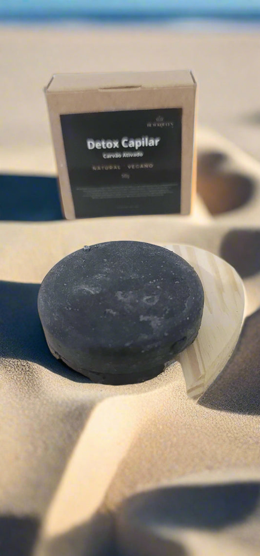 Black soap bar on a wooden board with a box labeled 'Detox Capilar' on a white background